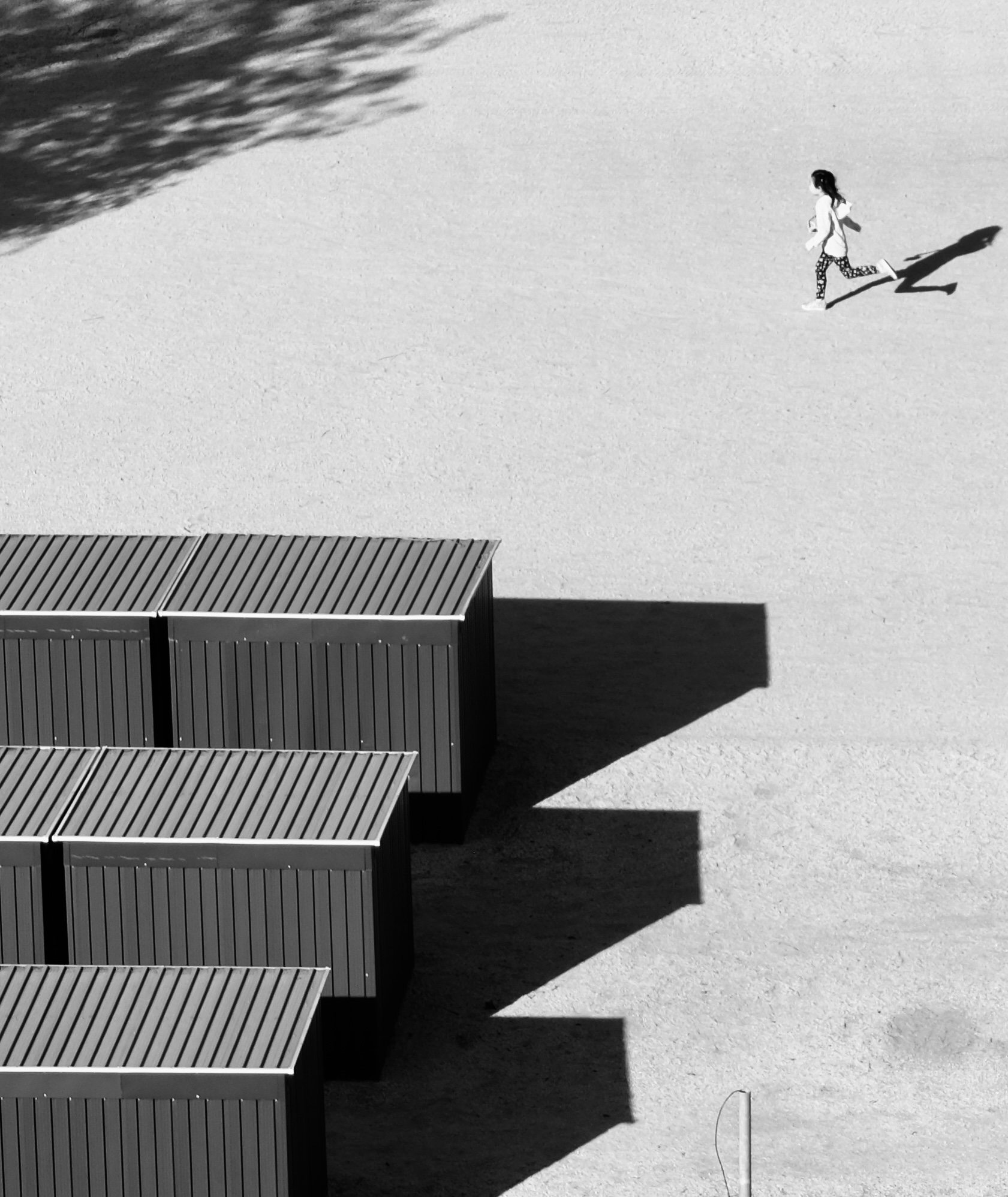 A lone runner crossing a vast sunlit plaza, seen from above
